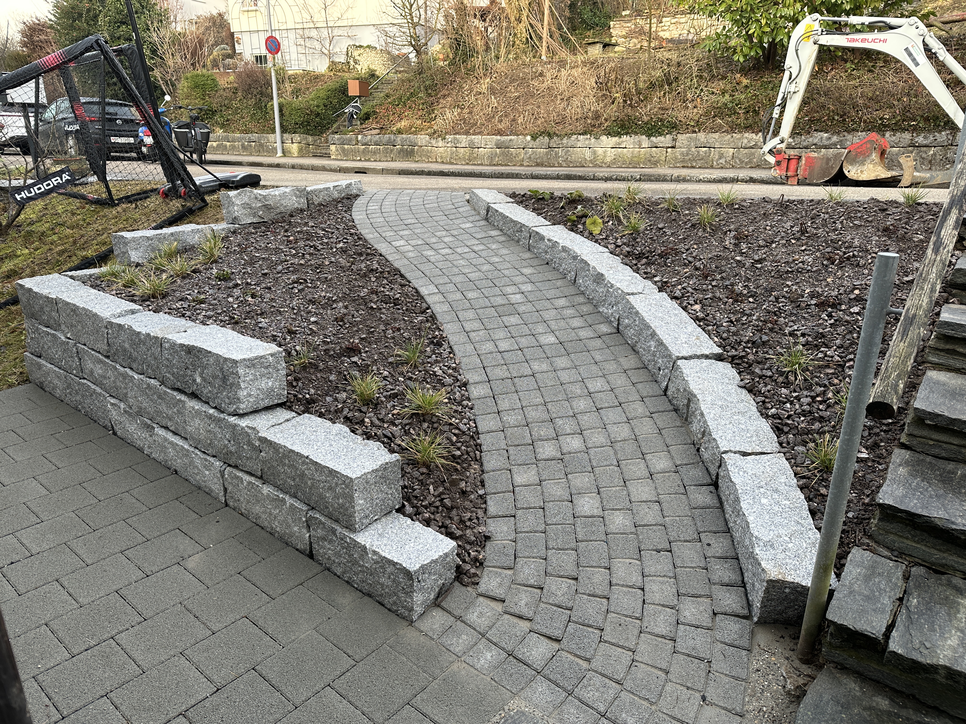 Geschwungener Kopfsteinpflasterweg mit beidseitiger Granitmauer