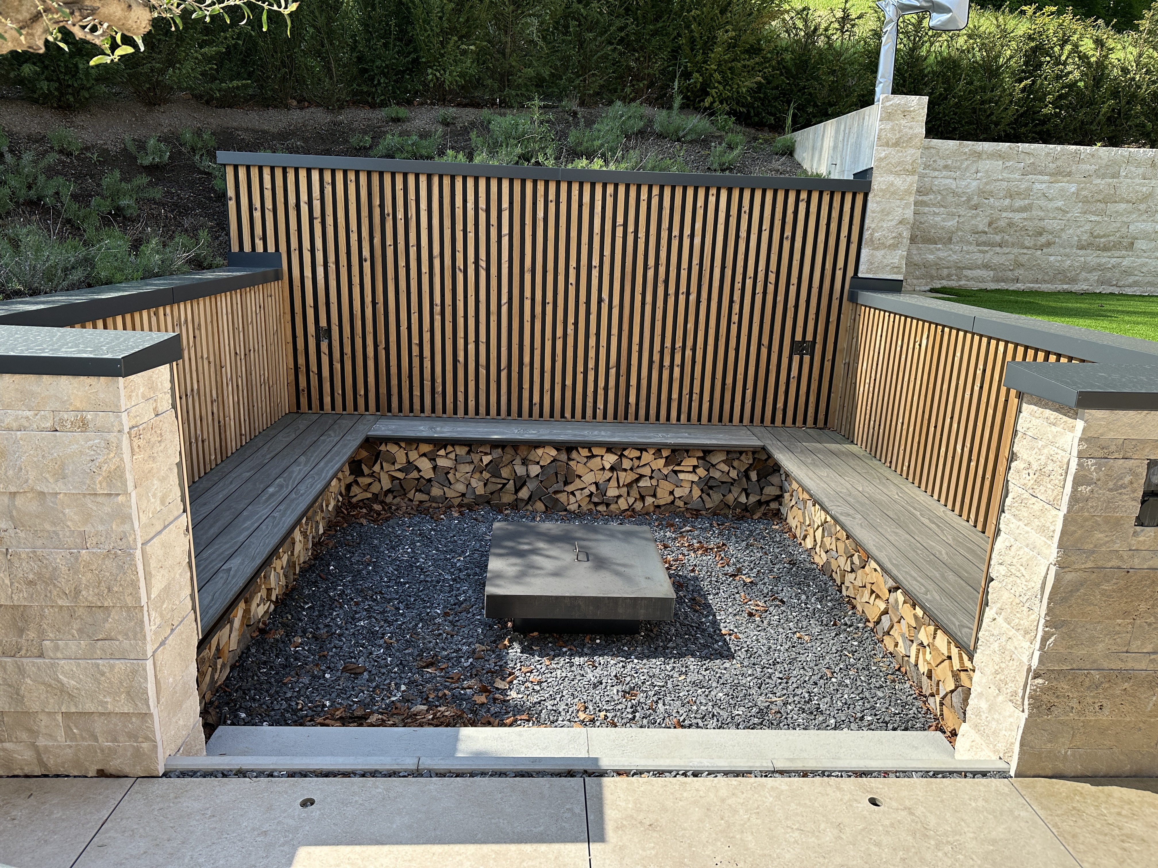 Outdoor-Lounge mit Feuerstelle, Holzwand und Natursteinmauer
