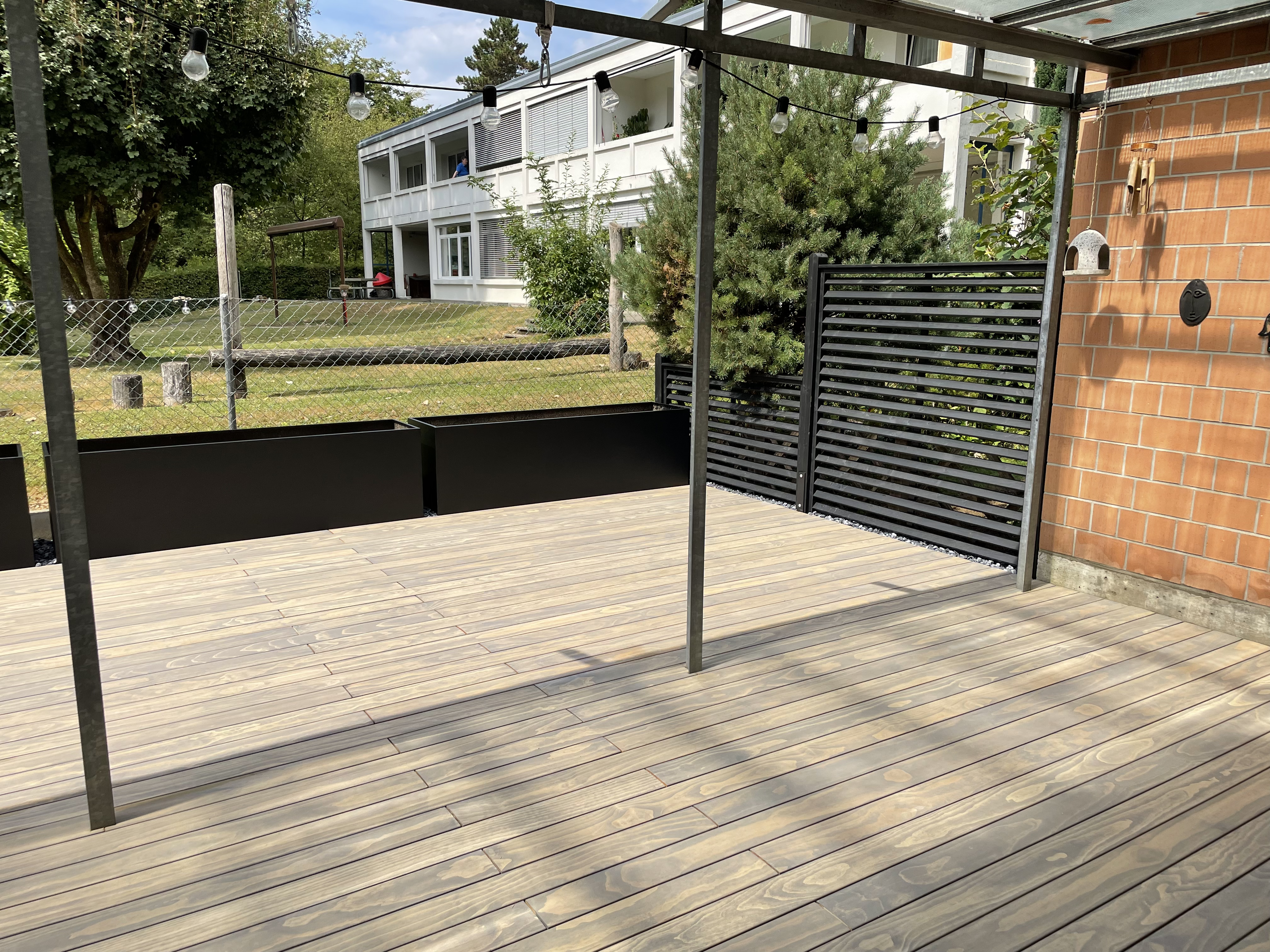 Holzterrasse mit Pergola, Hochbeeten und Lichterketten