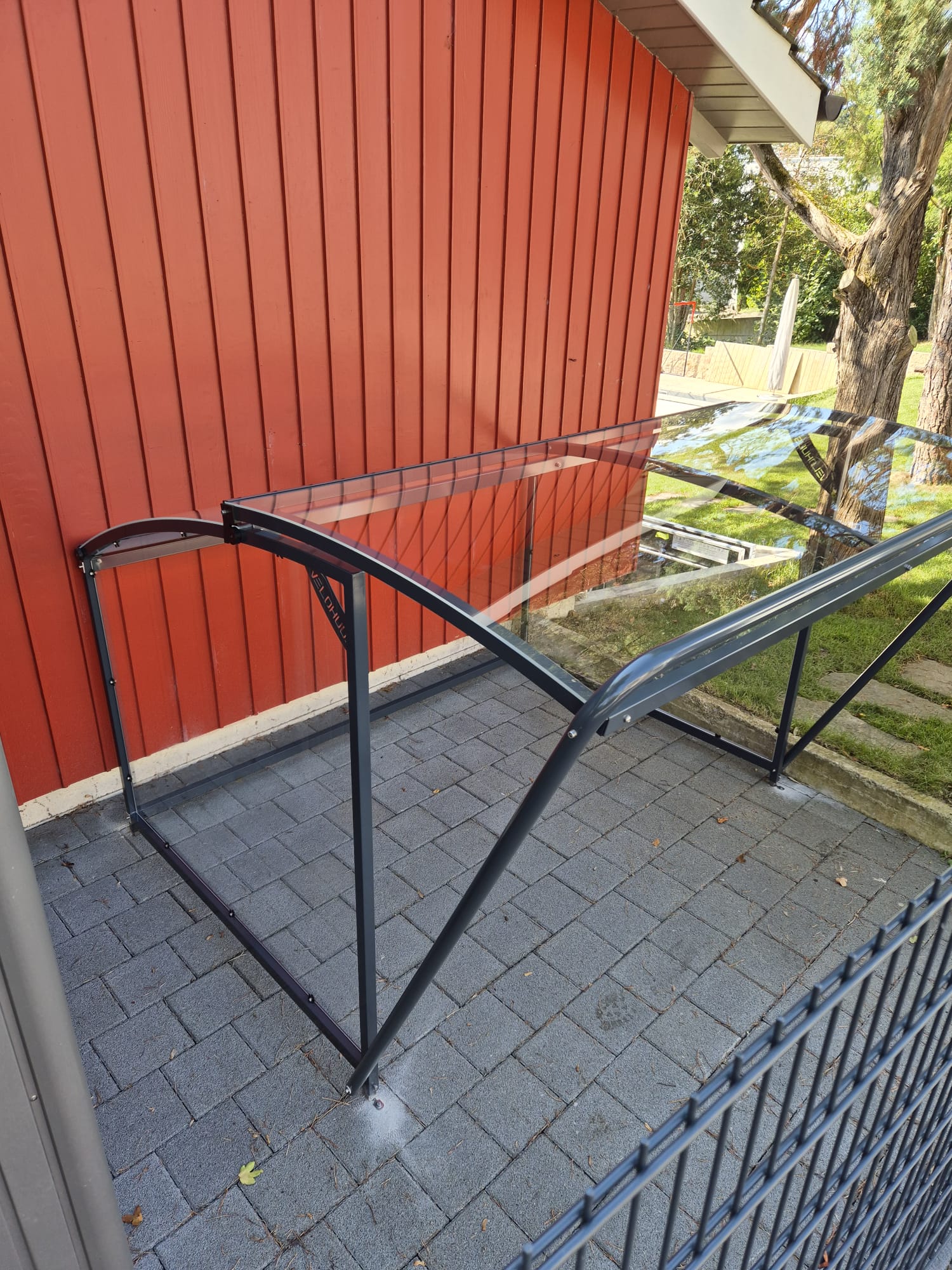 Velounterstand mit Glasdach an roter Fassade